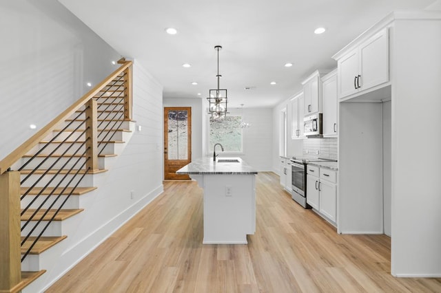 kitchen with light wood-type flooring, light stone counters, stainless steel appliances, a center island with sink, and white cabinets