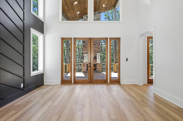 foyer entrance with light wood-type flooring, a towering ceiling, wood ceiling, and french doors