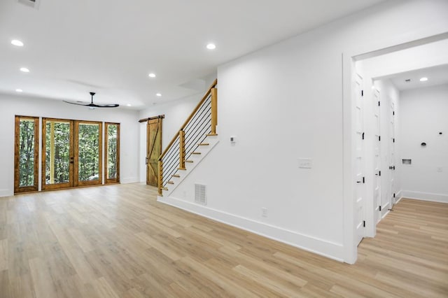 unfurnished living room featuring ceiling fan, a barn door, and light hardwood / wood-style flooring