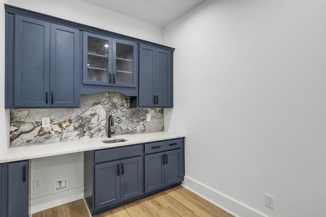 bar featuring light hardwood / wood-style floors, blue cabinets, tasteful backsplash, and sink