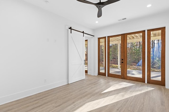 spare room featuring ceiling fan, a barn door, french doors, and light hardwood / wood-style flooring