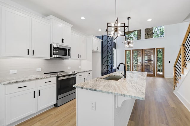 kitchen featuring white cabinetry, sink, decorative light fixtures, a kitchen island with sink, and appliances with stainless steel finishes