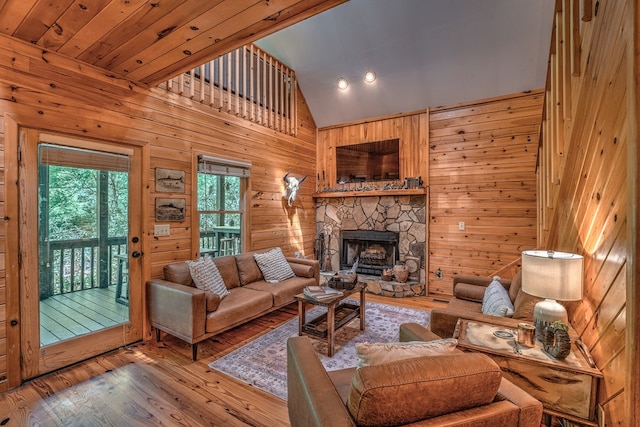 living area with high vaulted ceiling, wood walls, a stone fireplace, and wood finished floors