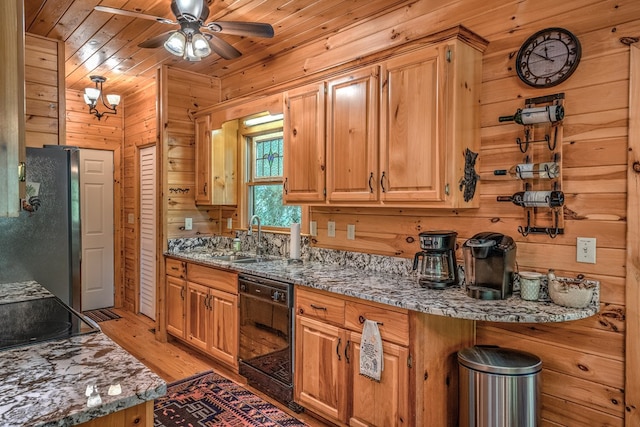 kitchen with dishwasher, wood walls, a sink, and freestanding refrigerator