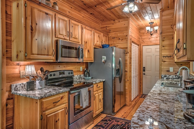 kitchen with wooden walls, stainless steel appliances, a sink, brown cabinets, and dark stone counters