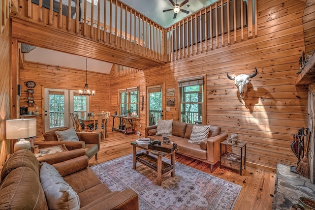 living room with a towering ceiling, wooden walls, light wood finished floors, and ceiling fan with notable chandelier