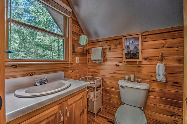 bathroom with vaulted ceiling, wooden walls, toilet, and vanity