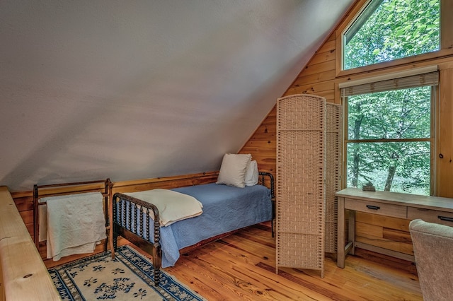 bedroom featuring lofted ceiling, wooden walls, a textured ceiling, and wood finished floors