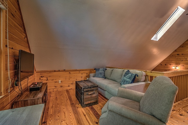 living room featuring a wainscoted wall, vaulted ceiling with skylight, wood walls, and light wood-type flooring