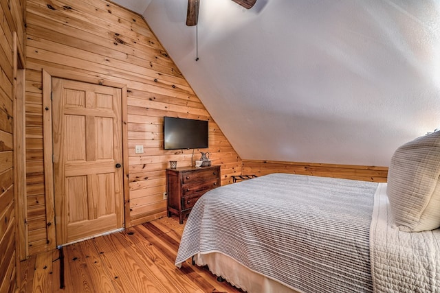 bedroom with vaulted ceiling, light wood-type flooring, a ceiling fan, and wooden walls