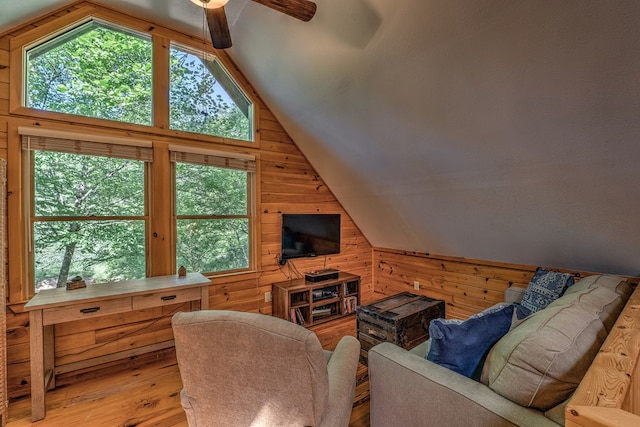 living area with lofted ceiling, a healthy amount of sunlight, wooden walls, and wood finished floors