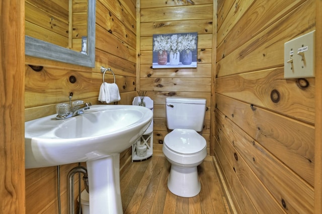 half bathroom with toilet, wood finished floors, and wood walls