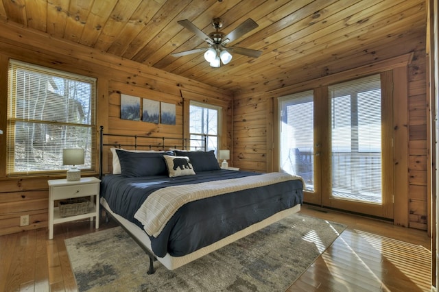 bedroom featuring hardwood / wood-style flooring, access to outside, wooden ceiling, wood walls, and ceiling fan