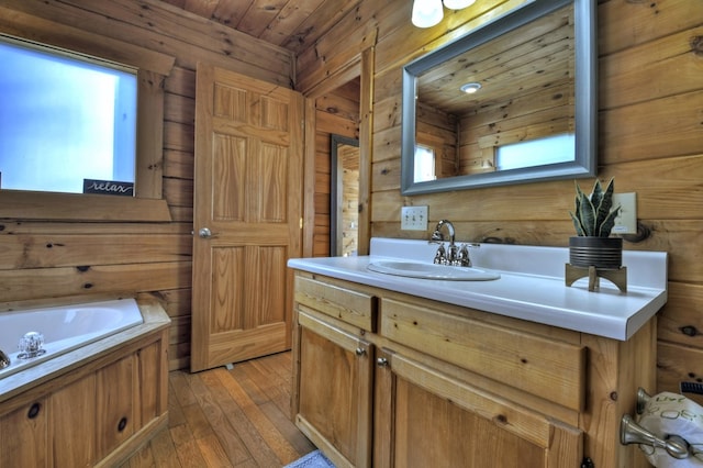 bathroom with a garden tub, hardwood / wood-style floors, wooden ceiling, wood walls, and vanity