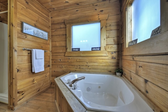 bathroom featuring a tub with jets, wooden walls, and wood finished floors