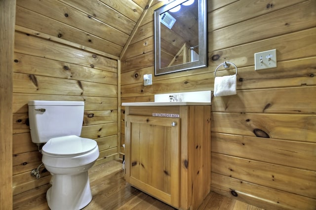 bathroom with vanity, wood finished floors, lofted ceiling, wood walls, and toilet