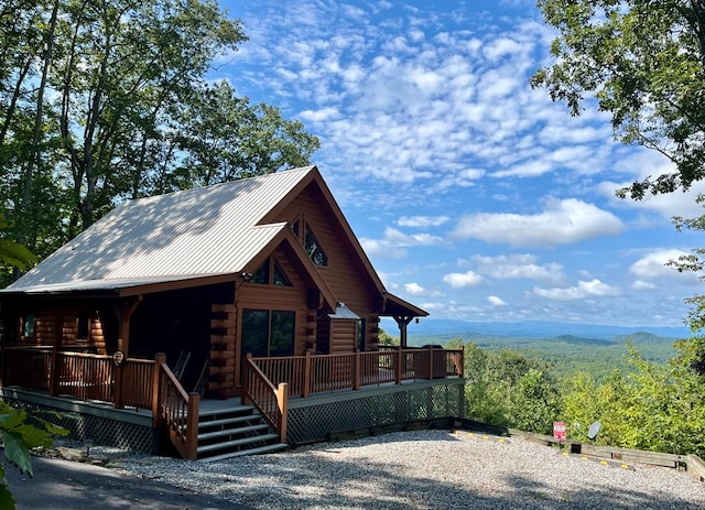 log cabin featuring a wooden deck, log siding, a view of trees, and metal roof