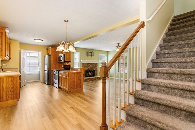 421 Burgess Rd, Ellijay, GA 30540 - kitchen with appliances with stainless steel finishes, open floor plan, brown cabinetry, a warm lit fireplace, and light wood-type flooring