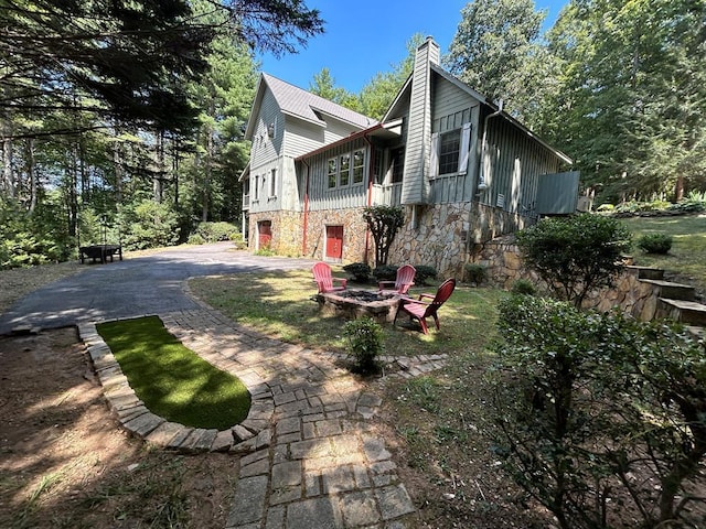 view of property exterior featuring aphalt driveway, a fire pit, stone siding, and a chimney