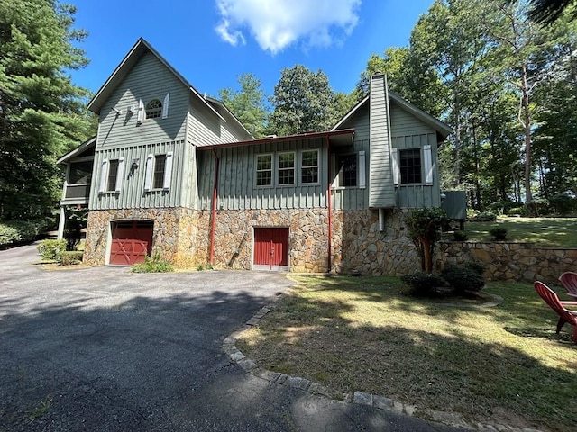 view of front of property with driveway, stone siding, a chimney, an attached garage, and board and batten siding