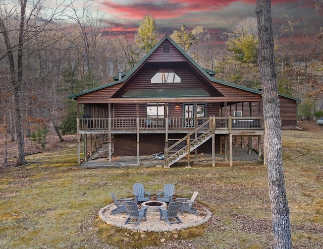 back of property at dusk featuring an outdoor fire pit, a yard, a wooden deck, and stairs