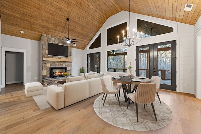 dining room with french doors, a stone fireplace, high vaulted ceiling, light hardwood / wood-style floors, and ceiling fan with notable chandelier