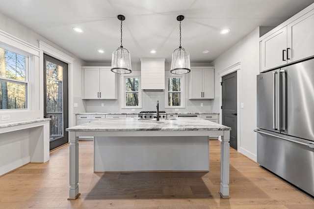 kitchen featuring white cabinetry, light stone counters, a kitchen island with sink, high end fridge, and custom exhaust hood