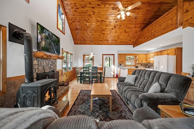 living room with a wood stove, high vaulted ceiling, light hardwood / wood-style flooring, and ceiling fan