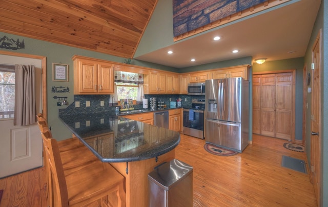 kitchen with stainless steel appliances, backsplash, kitchen peninsula, lofted ceiling, and light hardwood / wood-style flooring