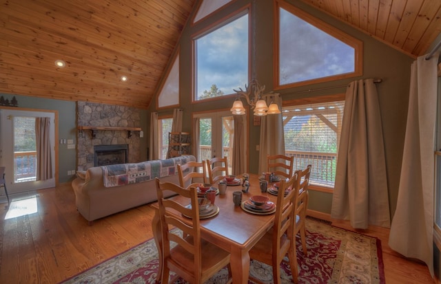 dining space with a stone fireplace, light wood-type flooring, plenty of natural light, and wooden ceiling