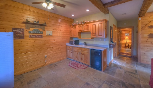 kitchen featuring wood walls, sink, ceiling fan, and beam ceiling