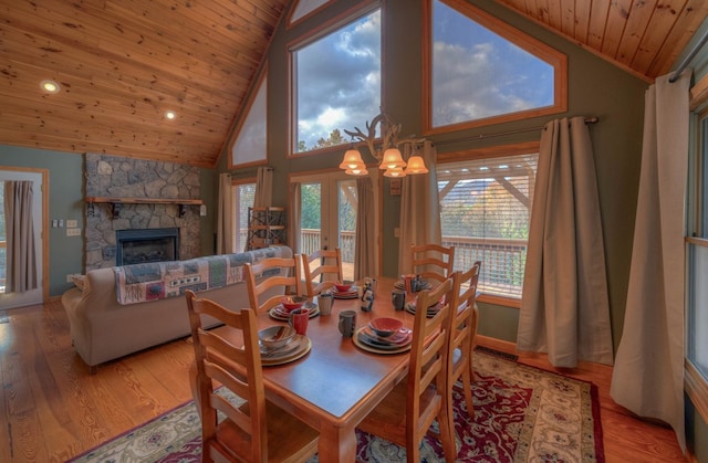 dining area featuring a stone fireplace, light wood-type flooring, a wealth of natural light, and wooden ceiling