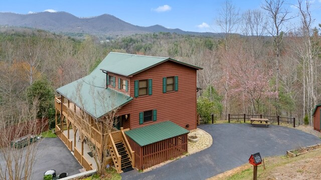 chalet / cabin with a mountain view, a wooded view, driveway, stairs, and metal roof