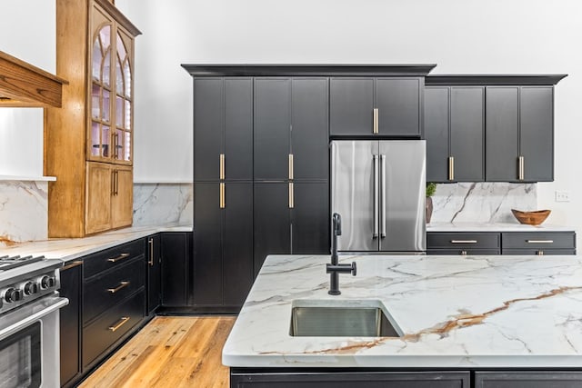 kitchen with sink, light hardwood / wood-style flooring, backsplash, light stone counters, and premium appliances