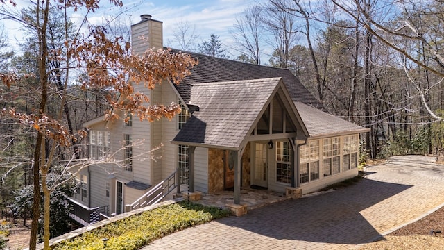 view of home's exterior with roof with shingles, a chimney, and a sunroom