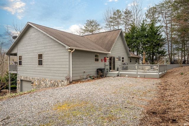 exterior space with an attached garage, a shingled roof, gravel driveway, and a wooden deck