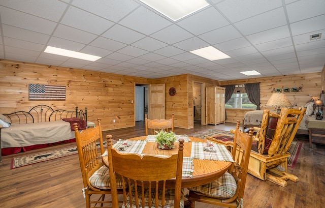 dining area with a drop ceiling, wood finished floors, visible vents, and wooden walls