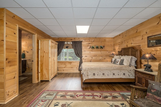 bedroom with a paneled ceiling, wood walls, and wood finished floors