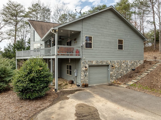 back of property with roof with shingles, a ceiling fan, a garage, stone siding, and driveway