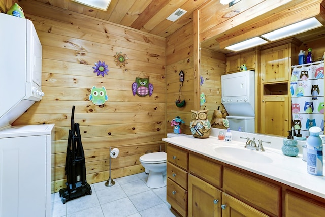 bathroom with vanity, tile patterned floors, stacked washer and dryer, wooden walls, and toilet