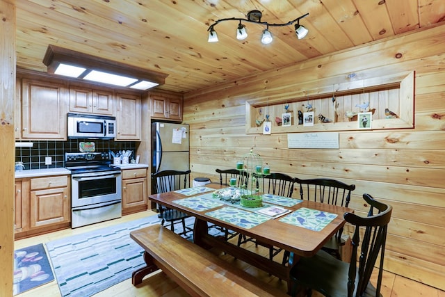 dining room with light wood-type flooring, wooden ceiling, and wood walls