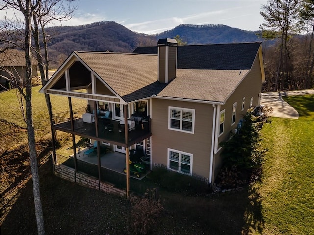 rear view of property featuring a shingled roof, a patio, a balcony, a chimney, and a mountain view