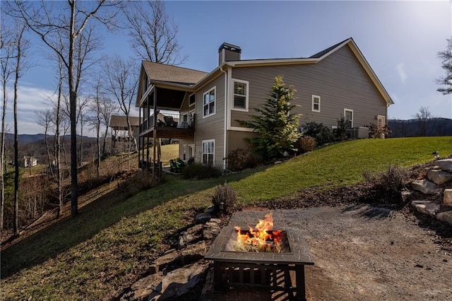 back of house with an outdoor fire pit, a lawn, and a chimney