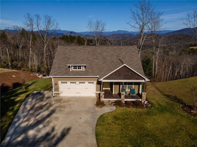 view of front facade featuring a shingled roof, covered porch, concrete driveway, a mountain view, and a front lawn