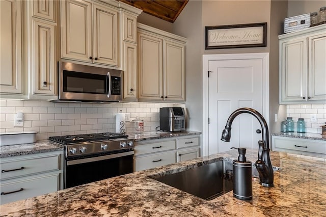 kitchen with a sink, appliances with stainless steel finishes, light stone counters, and cream cabinetry