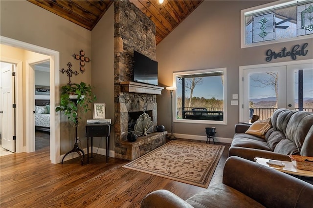 living room featuring a wealth of natural light, wood ceiling, wood finished floors, and a stone fireplace