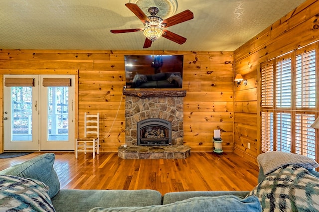 living room featuring a fireplace, wood-type flooring, ceiling fan, wooden walls, and a textured ceiling