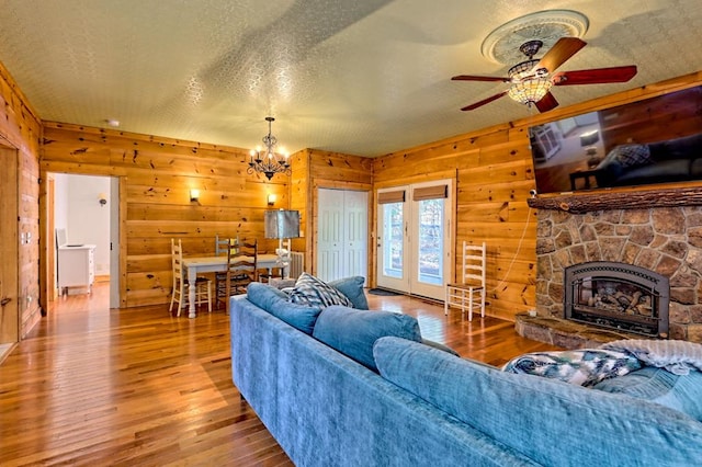 living area with a fireplace, wood-type flooring, wooden walls, a textured ceiling, and ceiling fan with notable chandelier