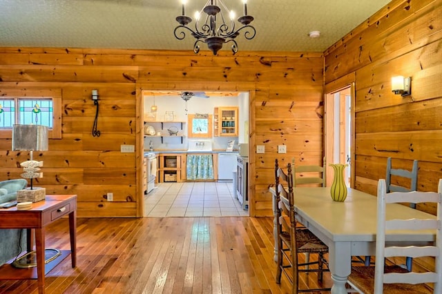 dining room with light wood-style floors, wooden walls, and a chandelier