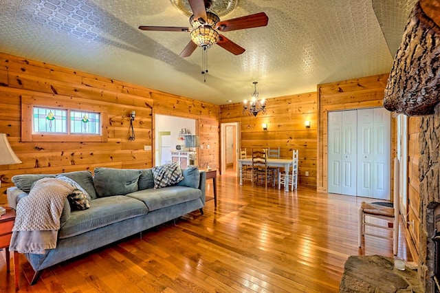 living area with wooden walls, a textured ceiling, hardwood / wood-style floors, and ceiling fan with notable chandelier